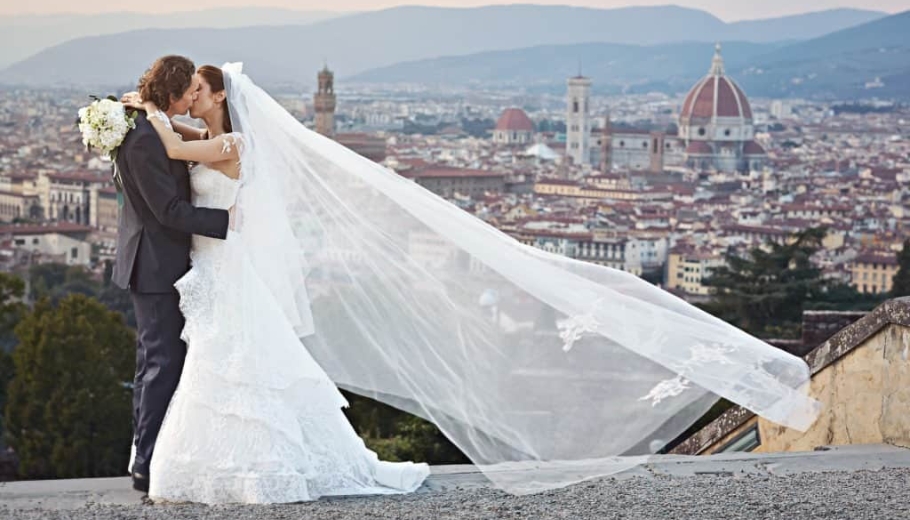 The bride and groom share a kiss with Florence's cityscape in the background, highlighting their destination wedding at Piazzale Michelangelo.