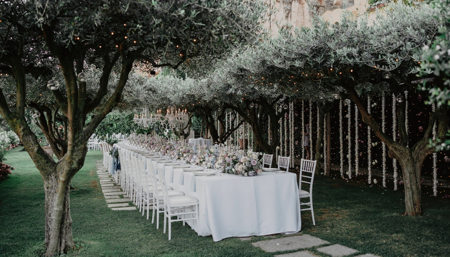 An outdoor wedding reception featuring white tables and chairs set up for guests, highlighting a destination wedding theme.