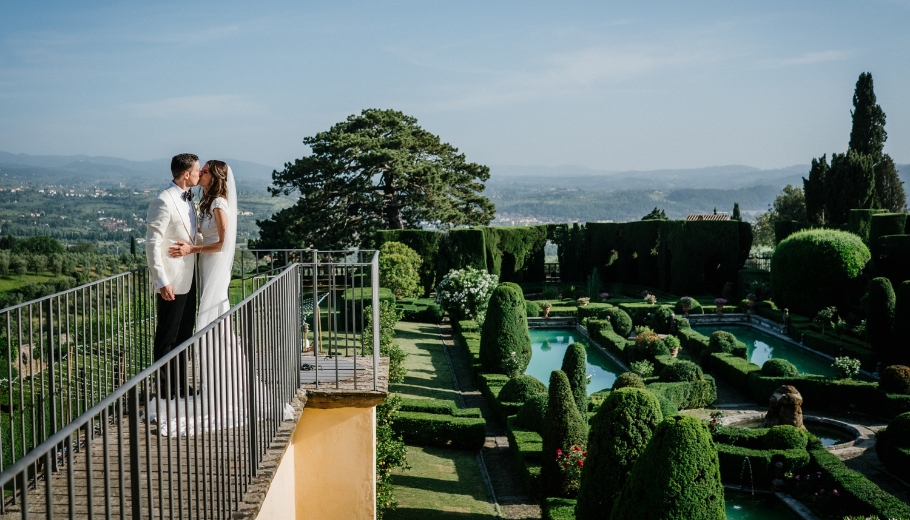 A wedding photographer takes photos of a couple at Villa Gamberaia, a stunning villa in Tuscany, Italy, amidst beautiful landscapes.