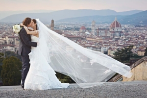 Bride and groom kissing each other on Piazzale Michelangelo, a terrace overlooking Florence. The
veil of the bride flows in the wind.