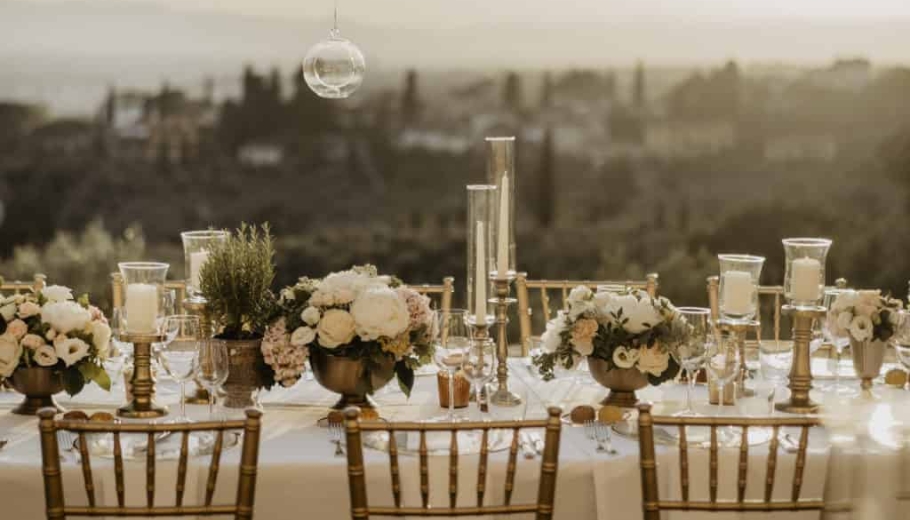 Italian Wedding Planners are set up Wedding table decorated with golden chairs, white candles, flowers and glassed bulbs
