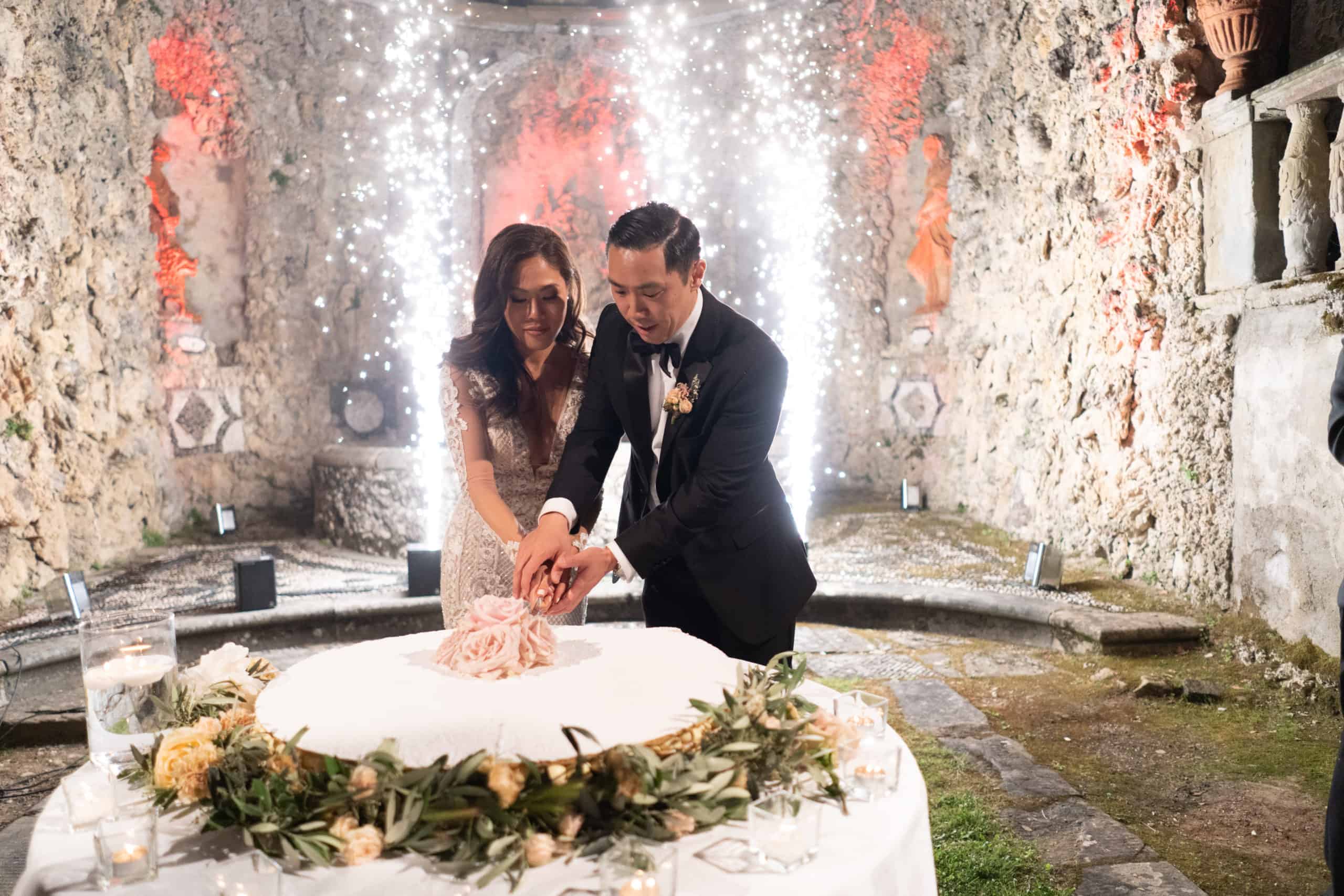 Bride and Groom cutting the wedding cake while having cold fireworks shining