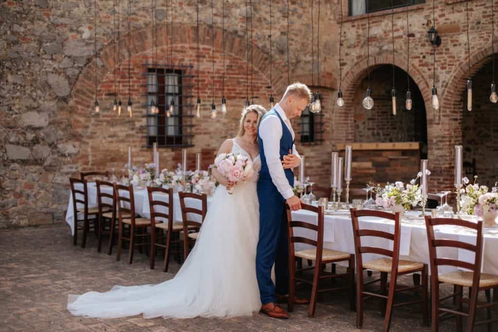 The bride and groom are in the courtyard of an ancient villa, near a decorated table 