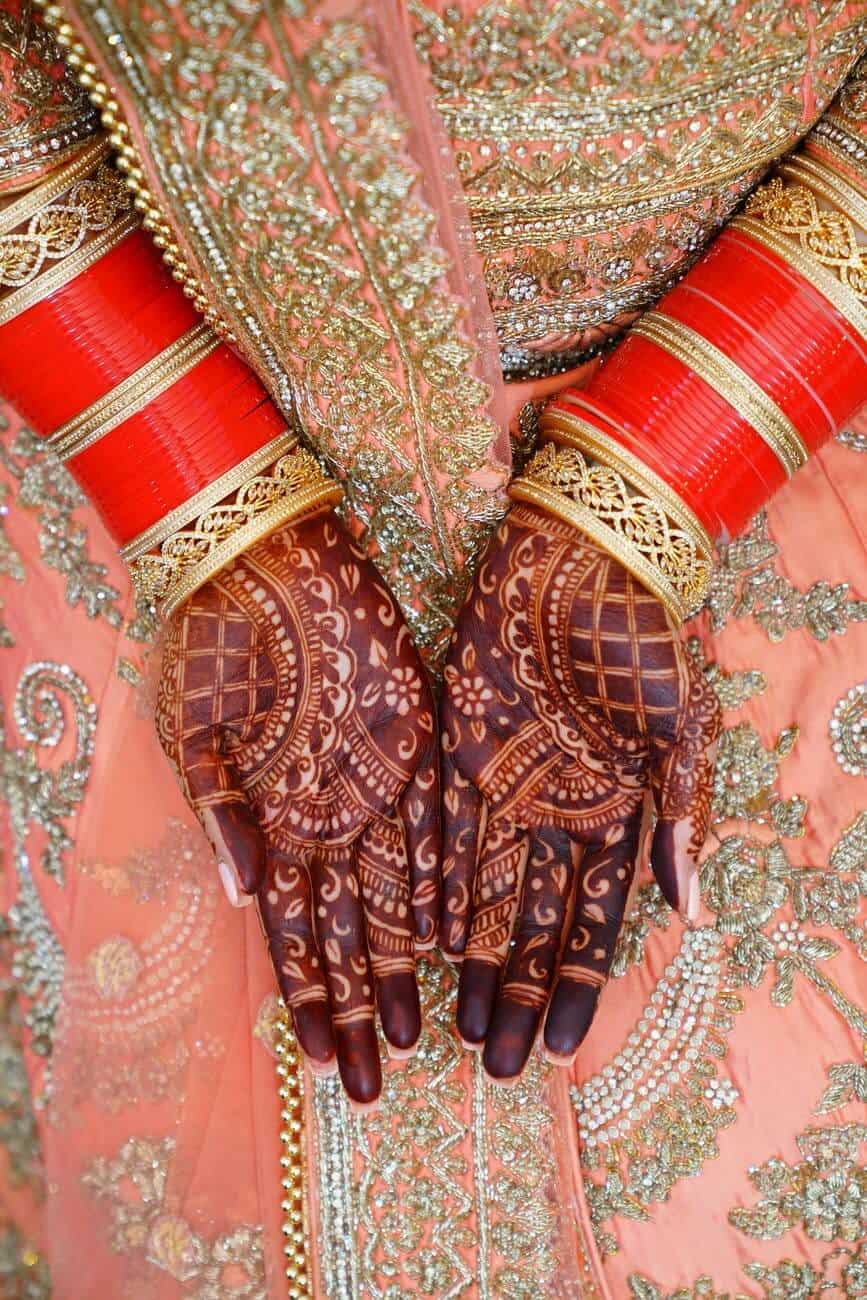 hindu brides hands with mehndi tattoes wears red and gold bracelets