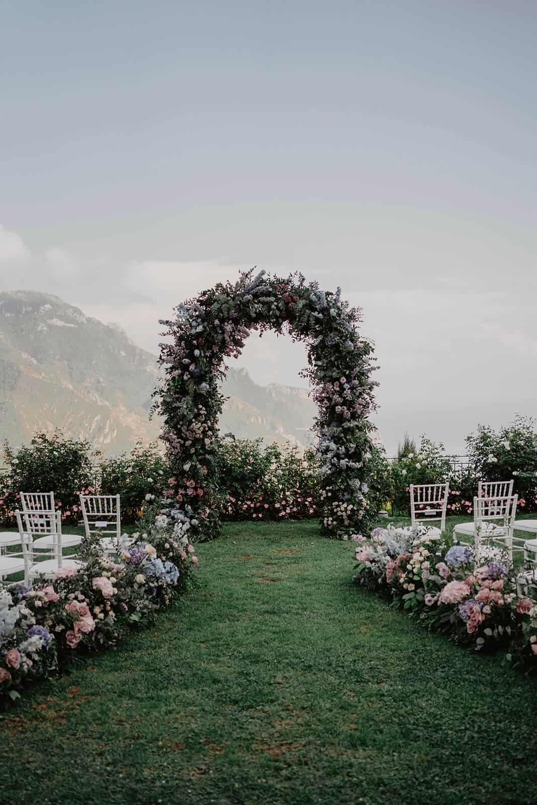garden wedding with an archway full of seasonal flowers and white chairs