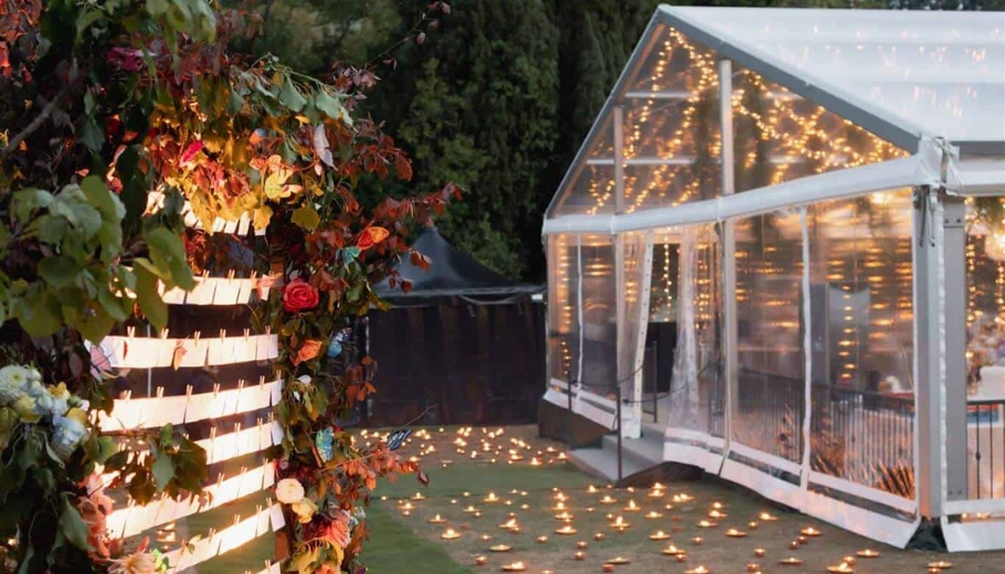 A beautifully decorated wedding tent illuminated with string lights and candles, creating a romantic atmosphere for guests.