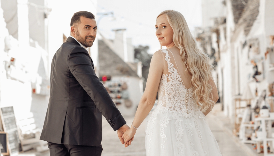 The bride and groom walk together along a picturesque street, highlighting their wedding outfits and unique hairstyles.