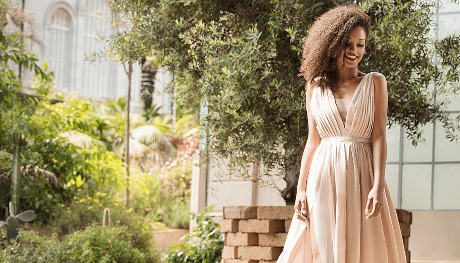 A woman in a flowing dress strolls along a sidewalk, highlighting her elegant side-swept au naturel wedding hairstyle.