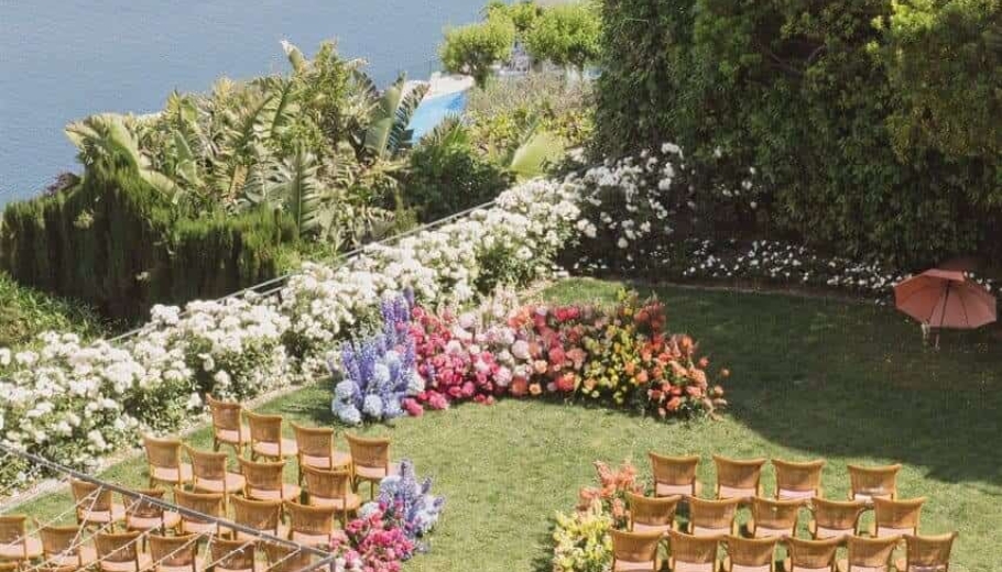 Outdoor wedding ceremony set in a garden, featuring rows of chairs adorned with flowers and a festive atmosphere.