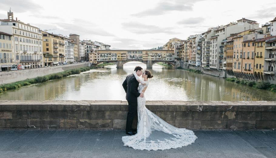 A couple embraces with an Italian cityscape backdrop, symbolizing marriage abroad.