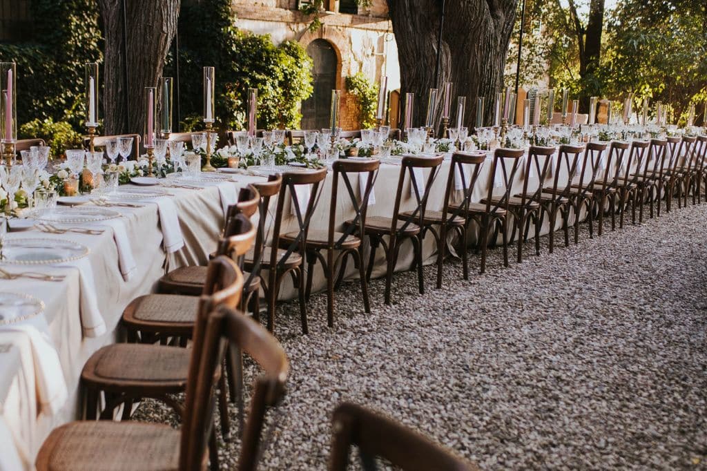 A rustic Italian wedding reception setup with a long, elegant table under a canopy of trees.