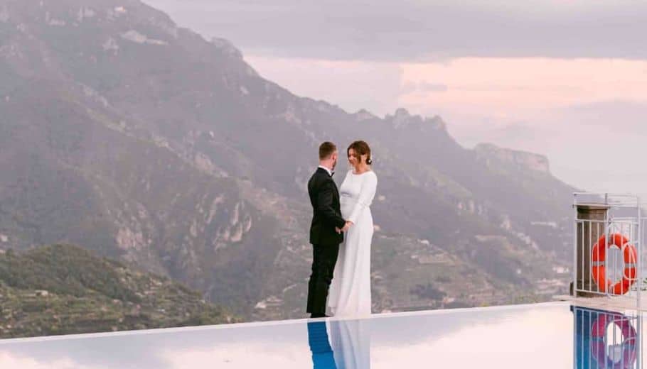 The Corilee & Will pose at a pool's edge, with mountains in the background, embracing their Italian wedding traditions.