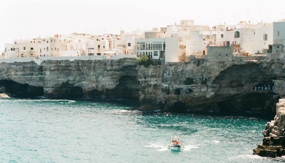 A boat navigates the water adjacent to a cliff, embodying the picturesque allure of Puglia and its rich Italian wedding traditions.