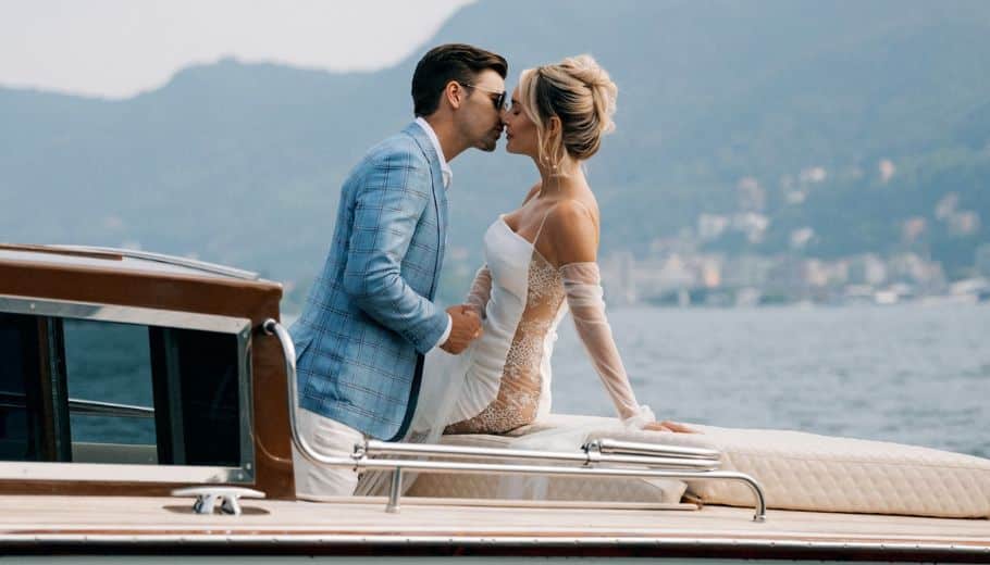 Bride and groom share a kiss on a boat with Lake Como's serene waters behind.