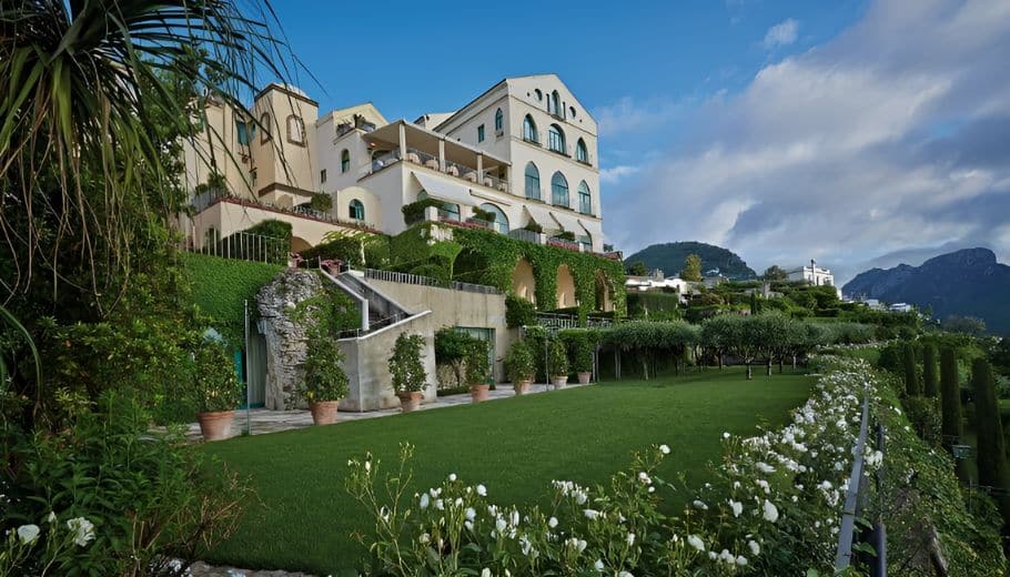 A stunning villa at Caruso, a Belmond Hotel, enveloped by vibrant green plants and colorful flowers.