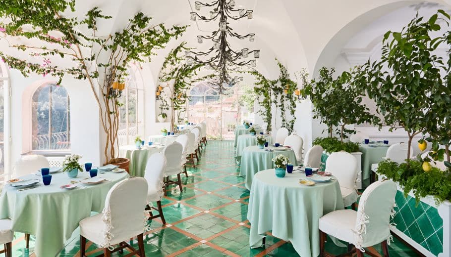 A picturesque wedding venue on the Amalfi Coast, showcasing green and white tables and chairs in a lovely restaurant setting.