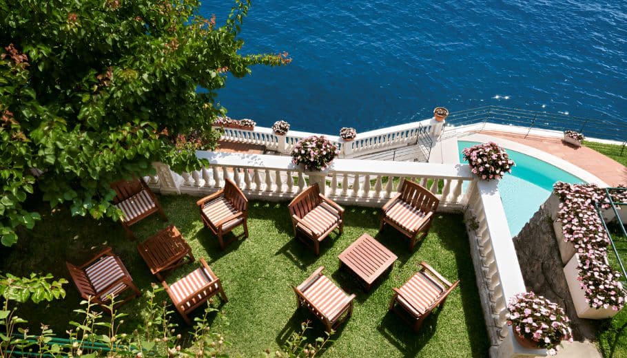 A serene lawn at Palazzo Avino, featuring chairs and tables with a stunning view of the ocean on the Amalfi Coast.