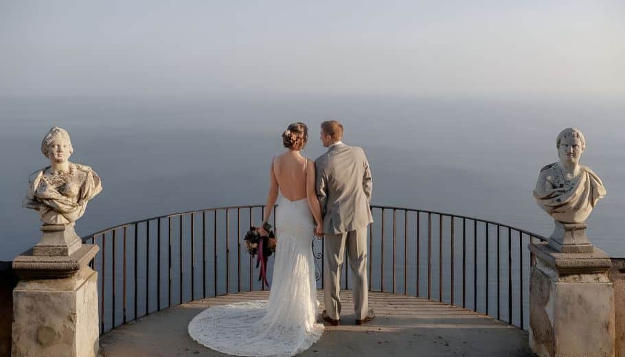 A bride and groom on a balcony at Villa Cimbrone, overlooking the stunning Amalfi Coast ocean view.