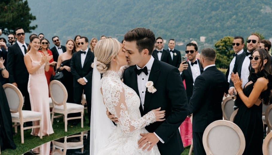 A bride and groom share a kiss during their elegant Lake Como wedding, surrounded by guests in a picturesque outdoor setting.